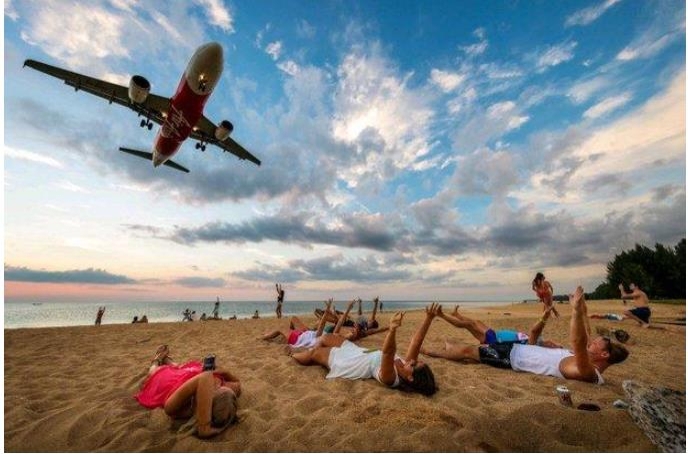 푸껫 마이 카오 해변에서 착륙 중인 항공기를 배경으로 사진을 찍는 관광객들