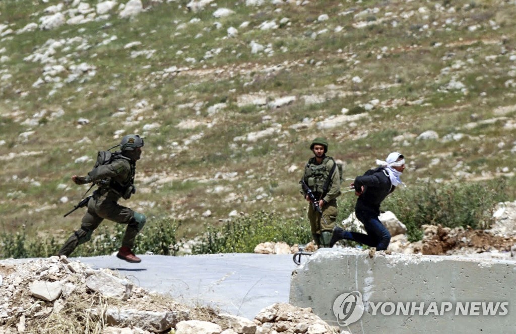 지난 18일(현지시간) 팔레스타인 소년 오사마 알바단(오른쪽)이 눈을 가리고 손이 묶인채 이스라엘 군인들로부터 도망치는 모습 [Photo by MOHAMMED HMEID / AFP=연합뉴스]