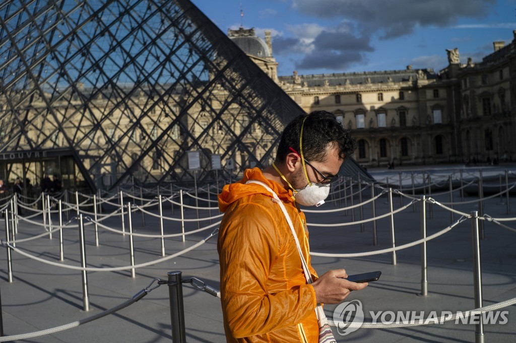 13일 파리 루브르 박물관 중앙정원에 마스크를 쓴 시민이 스마트폰을 들여다보고 있다. [EPA=연합뉴스]