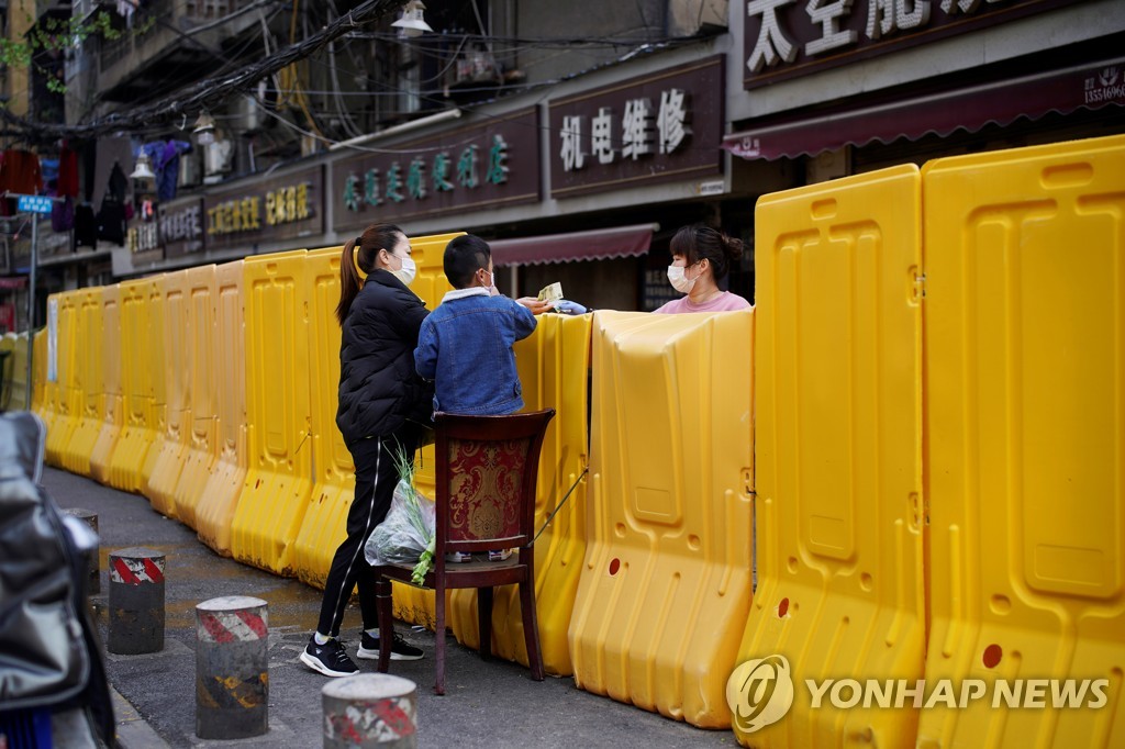 1일 우한에서 마스크를 쓴 한 여성이 건물 봉쇄 장벽 너머로 채소를 사고 있다. [로이터=연합뉴스]