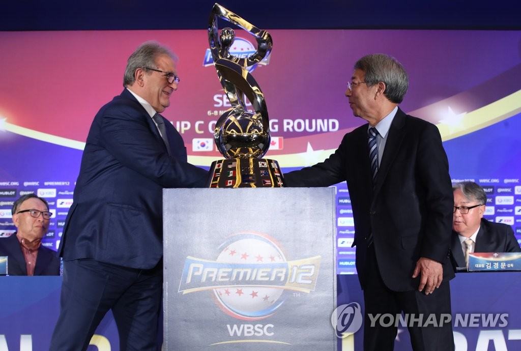 Riccardo Fraccari (L), president of the World Baseball Softball Confederation, Chung Un-chan, commissioner of the Korea Baseball Organization, shake hands behind the championship trophy for the Premier 12 tournament during a press conference announcing the competition's schedule in Seoul on April 15, 2019. (Yonhap)
