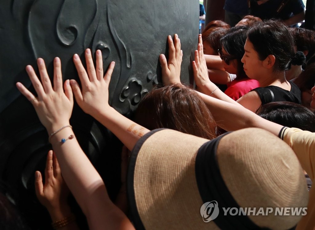 Parents of students who are seniors in high school touch the bell at Bosingak in central Seoul on Aug. 6, 2019, 100 days ahead of this year's college entrance exam, praying for their children. (Yonhap)