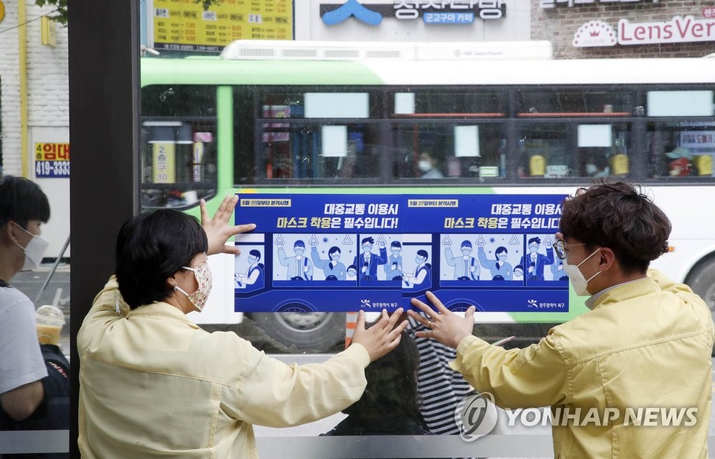 This photo, provided by the office of Gwangju Buk Ward on May 25, 2020, shows officials putting up notices about wearing face masks on public transportation at a bus stop near Chonnam National University in Gwangju. (Yonhap)