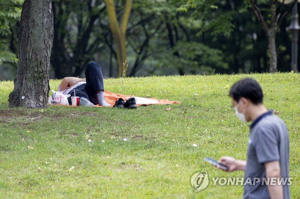 蒸し暑い日となった２日、ソウルの汝矣島公園の木陰で横になる市民＝（聯合ニュース）