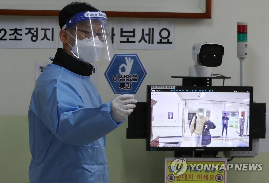 A teacher in quarantine gear checks students' body temperatures at a high school in Masan, South Gyeongsang Province, on Dec. 3, 2020, before the nationwide college entrance exam begins. (Yonhap)
