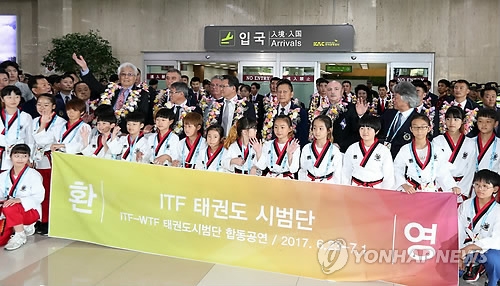 Officials and athletes of the North Korea-led International Taekwondo Federation stand behind South Korean youth taekwondo practitioners holding a welcome sign and wave to the crowd gathered at Gimpo International Airport in Seoul after their arrival on June 23, 2017. (Yonhap)