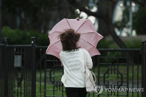 A pedestrian walks with her umbrella turned inside out due to strong wind in Seoul on May 18, 2020. (Yonhap)