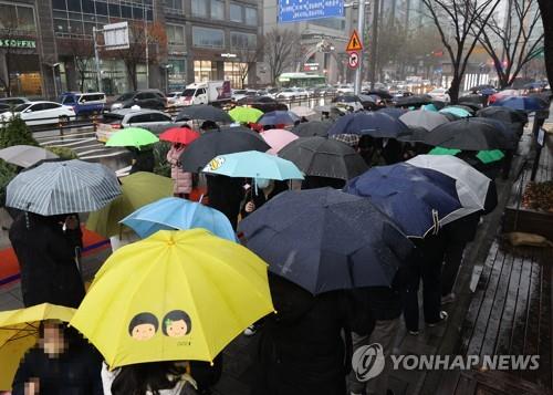 People stand in line in the rain to receive coronavirus tests at a screening clinic in Seoul's Songpa Ward on Nov. 30, 2021.