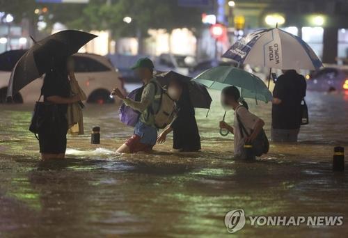 Los ciudadanos atraviesan una calle inundada en el distrito de Gangnam, en Seúl, el 8 de agosto de 2022, en medio de la mayor precipitación en el país en 80 años.