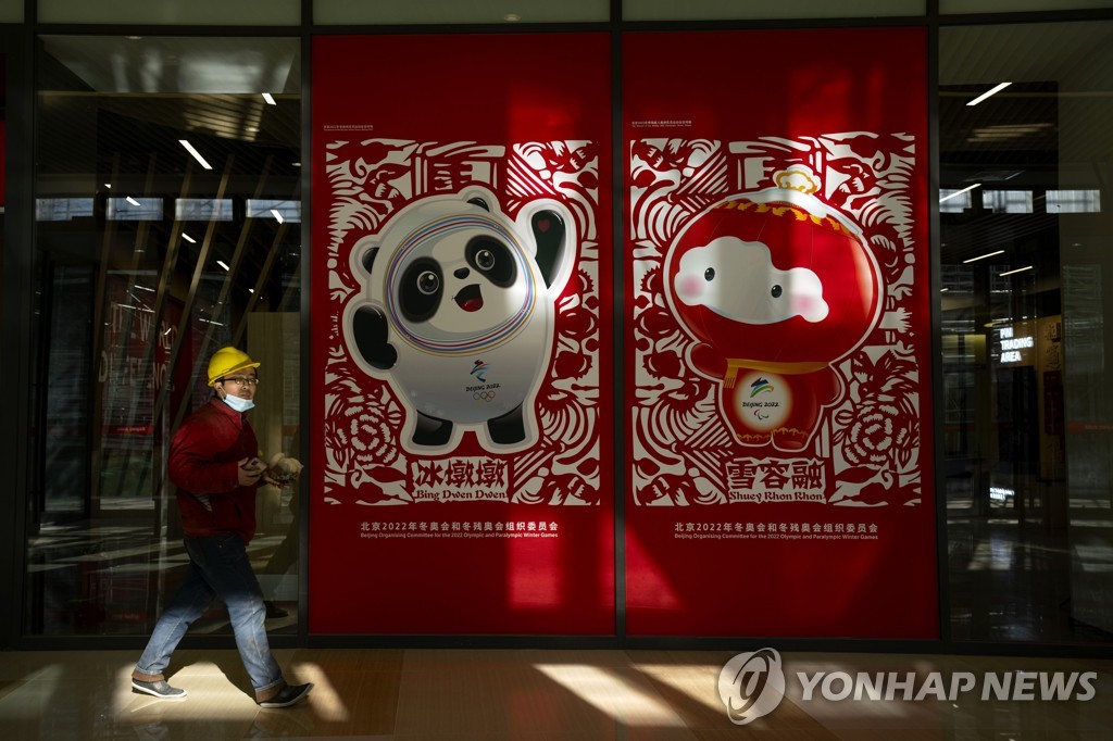 In this Associated Press photo, a worker walks past posters showing the 2022 Beijing Winter Olympics mascot Bing Dwen Dwen (L) and the Winter Paralympics mascot Shuey Rhon Rhon at a commercial plaza inside the Winter Olympic Village in Beijing on Dec. 24, 2021. (Yonhap)