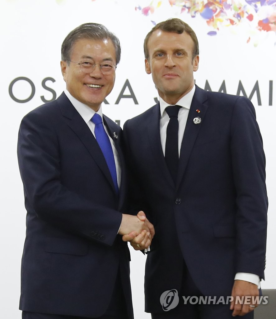 This file photo shows South Korean President Moon Jae-in (L) shaking hands with French President Emmanuel Macron during their talks on the margins of the Group of 20 summit in Osaka, Japan, on June 28, 2019. (Yonhap)