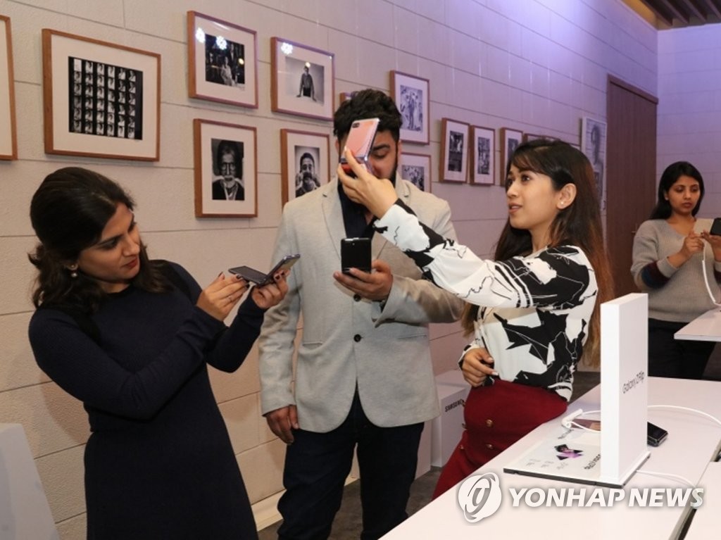 In this photo, provided by Samsung Electronics Co.'s Indian unit on Feb. 20, 2020, Indian consumers inspect the company's foldable smartphone, the Galaxy Z Flip, at an event in Gurugram, India. (PHOTO NOT FOR SALE) (Yonhap)