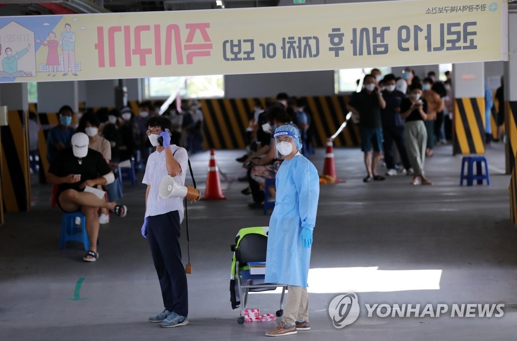 Health workers prepare to work as citizens wait in line at a virus screening clinic in Gwangju on Aug. 28, 2020. (Yonhap)