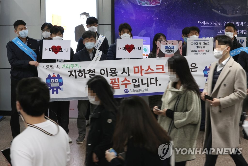 Seoul city officials hold signs calling for people to wear masks on the subway at Gwanghwamun Station in central Seoul on Nov. 13, 2020. (Yonhap)