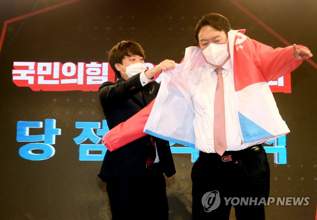 Lee Jun-seok (à gauche), chef du principal parti d'opposition, le Parti du pouvoir du peuple, aide l'ancien procureur général Yoon Seok-youl à enfiler une veste après avoir été élu candidat à la présidence du parti lors d'une convention nationale, au musée et à la bibliothèque Kim Koo à Séoul, le 5 novembre 2021.