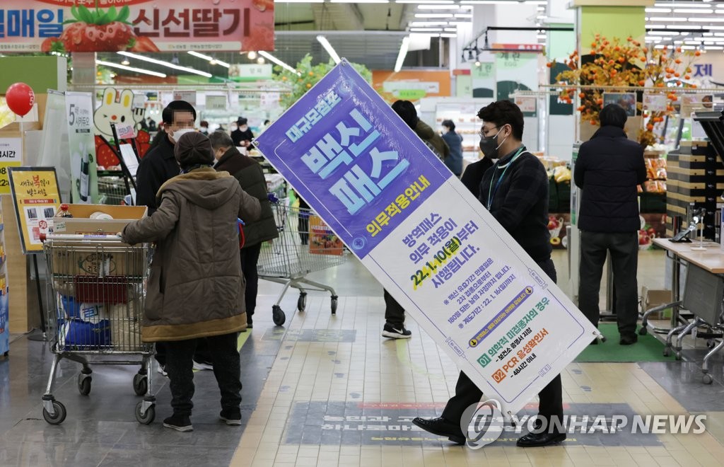 A clerk removes a notice on the government's mandatory vaccine pass system at a retail outlet in Seoul on Jan. 14, 2022, right after the Seoul Administrative Court suspended the vaccine pass at department stores and retail outlets located in Seoul. Restaurants and cafes were excluded from the suspension. (Yonhap)