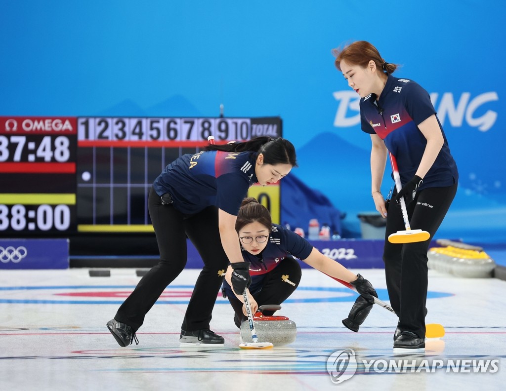 South Korean lead Kim Seon-yeong (C) throws the stone, with third Kim Kyeong-ae (L) sweeping the ice during the women's curling round robin game against Britain at the Beijing Winter Olympics at the National Aquatics Centre in Beijing on Feb. 11, 2022. (Yonhap)