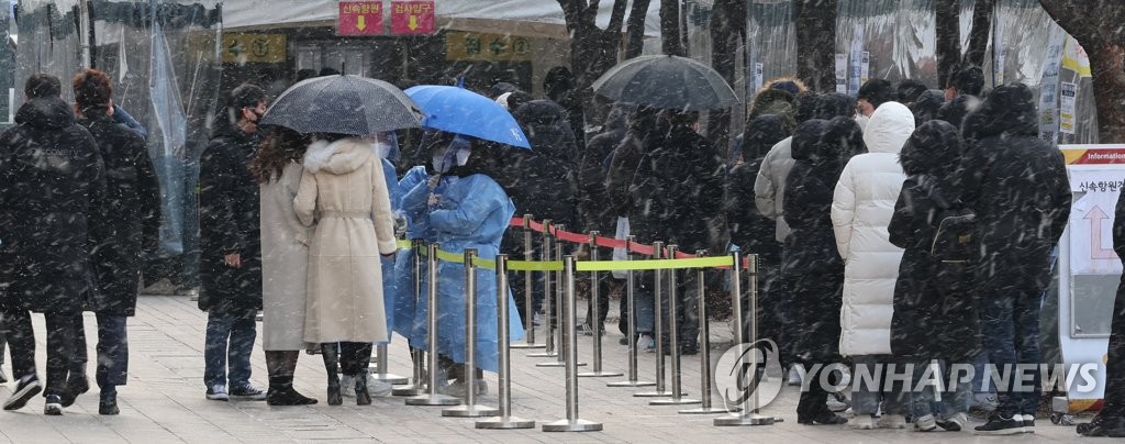People wait in line to receive tests at a COVID-19 testing station in Seoul on Feb. 15, 2022, as snow hits the capital city. South Korea's new daily cases hit a fresh high of 57,177 the same day. (Yonhap)