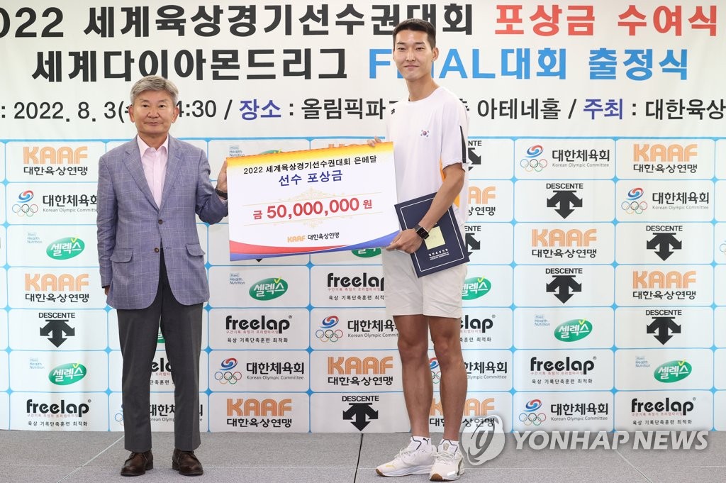 South Korean high jumper Woo Sang-hyeok (R) poses with an oversized check of 50 million won (US$38,150), awarded by the Korea Association of Athletics Federations President Lim Dai-ki (L), for winning silver at the World Athletics Championships, during a ceremony at Olympic Parktel in Seoul on Aug. 3, 2022. (Yonhap)