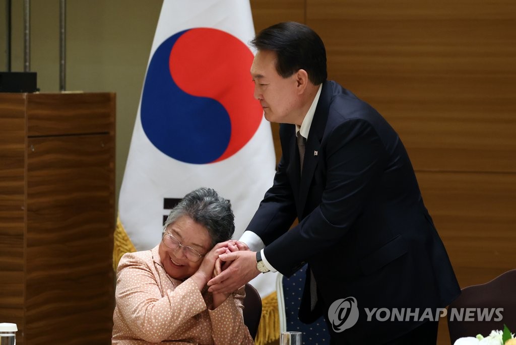 South Korean President Yoon Suk Yeol (R) holds hands with a Korean victim of the 1945 atomic bombing in Hiroshima, Japan, on May 19, 2023. (Pool photo) (Yonhap)